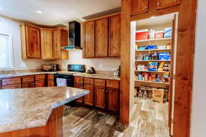 Kitchen with wall chimney exhaust hood, dark hardwood / wood-style floors, light stone counters, and black stove