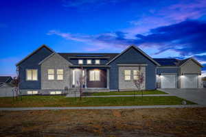 View of front facade featuring a lawn, a garage, and solar panels