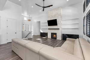 Living room featuring hardwood / wood-style floors, a fireplace, ceiling fan, and a high ceiling