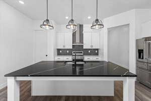 Kitchen with a spacious island, high end appliances, hanging light fixtures, and wall chimney range hood