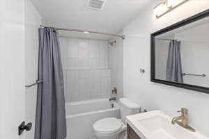 Full bathroom with toilet, shower / bath combo, vanity, and a textured ceiling