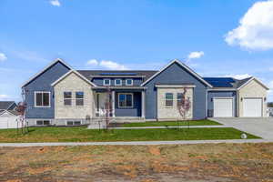 View of front of property with a garage, solar panels, and a front lawn