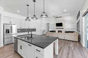 Kitchen with stainless steel appliances, decorative light fixtures, sink, an island with sink, and white cabinets