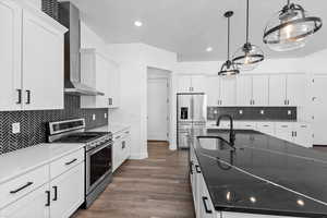 Kitchen featuring stainless steel appliances, wall chimney range hood, sink, white cabinets, and dark wood-type flooring