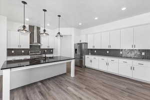 Kitchen with pendant lighting, wall chimney exhaust hood, sink, white cabinetry, and appliances with stainless steel finishes