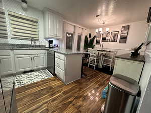 Kitchen with white cabinetry, stainless steel dishwasher, hanging light fixtures, and dark hardwood / wood-style floors