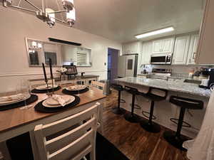 Kitchen with dark hardwood / wood-style flooring, stainless steel appliances, an inviting chandelier, tasteful backsplash, and light stone countertops