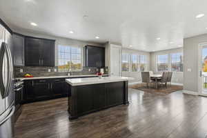 Kitchen featuring a textured ceiling, dark hardwood / wood-style floors, a kitchen island, backsplash, and appliances with stainless steel finishes