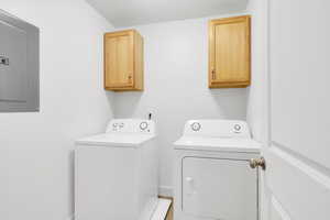 Washroom featuring electric panel, cabinets, and washing machine and clothes dryer