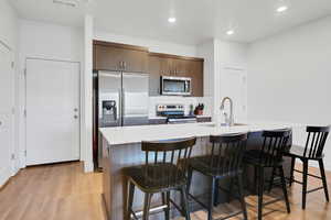 Kitchen with a kitchen bar, stainless steel appliances, sink, an island with sink, and light wood-type flooring