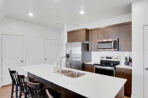 Kitchen featuring light hardwood / wood-style floors, a center island with sink, a breakfast bar, appliances with stainless steel finishes, and backsplash