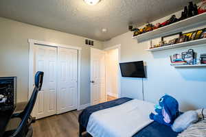 Bedroom featuring wood-type flooring, a textured ceiling, and a closet