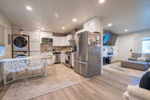 Kitchen featuring stacked washer and clothes dryer, white cabinetry, appliances with stainless steel finishes, and decorative backsplash