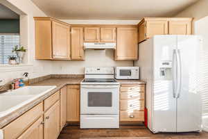 Kitchen featuring sink, light brown cabinetry, a textured ceiling, white appliances, and dark hardwood / wood-style flooring