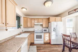 Kitchen with a textured ceiling, light brown cabinets, sink, dark wood-type flooring, and white appliances