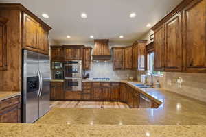 Kitchen featuring light stone counters, stainless steel appliances, sink, hardwood  floors, and custom exhaust hood, large walk-in pantry.