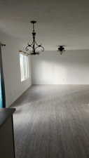 Empty room featuring a textured ceiling, light wood-type flooring, and a notable chandelier