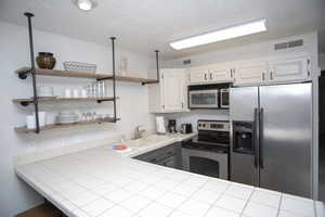 Kitchen featuring tile counters, white cabinets, hanging light fixtures, sink, and appliances with stainless steel finishes