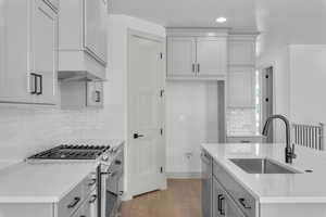 Kitchen with light stone counters, hardwood / wood-style floors, sink, tasteful backsplash, and appliances with stainless steel finishes