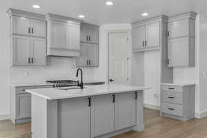 Kitchen featuring gray cabinets, decorative backsplash, light wood-type flooring, and an island with sink