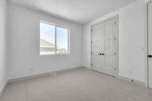 Unfurnished bedroom featuring a closet, a textured ceiling, and light carpet