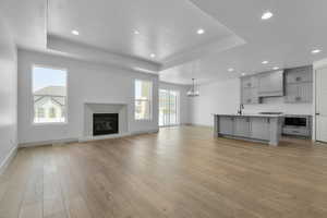 Unfurnished living room featuring a textured ceiling, light hardwood / wood-style flooring, a chandelier, and a raised ceiling