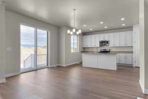 Kitchen with stainless steel appliances, white cabinetry, a center island with sink, decorative light fixtures, and hardwood / wood-style floors