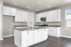 Kitchen with a kitchen island with sink, appliances with stainless steel finishes, dark wood-type flooring, and white cabinets