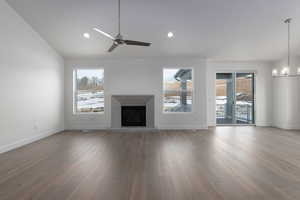 Unfurnished living room featuring hardwood / wood-style floors, ceiling fan with notable chandelier, and plenty of natural light