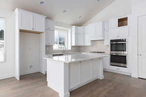 Kitchen with white cabinetry, stainless steel double oven, lofted ceiling, a kitchen island, and light wood-type flooring