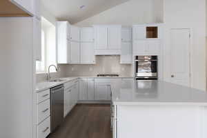 Kitchen featuring appliances with stainless steel finishes, dark hardwood / wood-style floors, a kitchen island, white cabinets, and vaulted ceiling