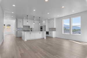 Kitchen featuring a kitchen island with sink, a mountain view, light hardwood / wood-style flooring, white cabinetry, and decorative light fixtures