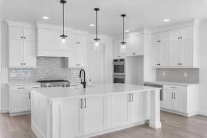 Kitchen featuring pendant lighting, white cabinets, and a kitchen island with sink