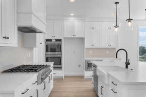 Kitchen featuring white cabinetry, appliances with stainless steel finishes, hanging light fixtures, light hardwood / wood-style floors, and custom exhaust hood