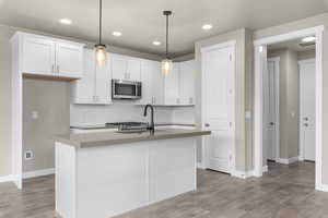 Kitchen featuring decorative backsplash, hardwood / wood-style flooring, a kitchen island with sink, white cabinetry, and decorative light fixtures