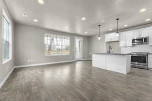 Kitchen with dark wood-type flooring, a kitchen island with sink, white cabinetry, appliances with stainless steel finishes, and decorative light fixtures