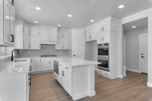 Kitchen with white cabinets, hardwood / wood-style floors, sink, a kitchen island, and appliances with stainless steel finishes