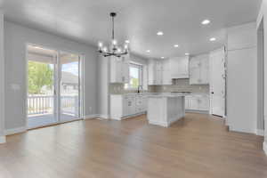 Kitchen with white cabinetry, backsplash, decorative light fixtures, light hardwood / wood-style floors, and a center island