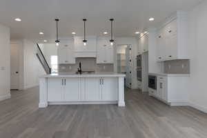 Kitchen featuring stainless steel appliances, white cabinetry, pendant lighting, and light hardwood / wood-style flooring