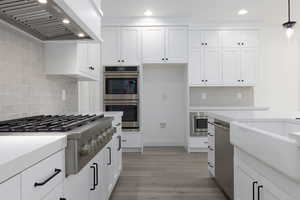 Kitchen with stainless steel appliances, wall chimney exhaust hood, decorative light fixtures, backsplash, and light wood-type flooring