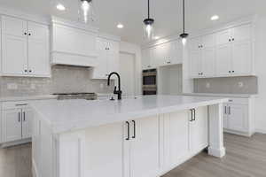 Kitchen featuring an island with sink, white cabinets, pendant lighting, and tasteful backsplash