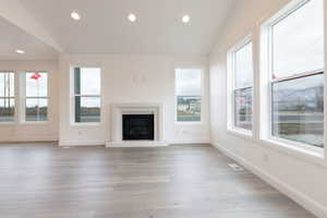 Unfurnished living room with light hardwood / wood-style floors, plenty of natural light, and vaulted ceiling