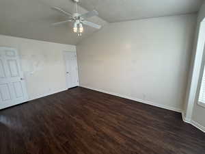 Empty room featuring a textured ceiling, dark wood-type flooring, ceiling fan, and vaulted ceiling