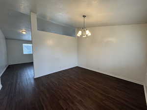 Unfurnished room featuring an inviting chandelier, lofted ceiling, a textured ceiling, and dark hardwood / wood-style floors