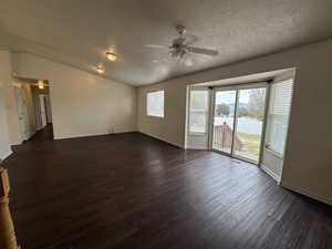 Empty room with dark wood-type flooring, lofted ceiling, a textured ceiling, and ceiling fan