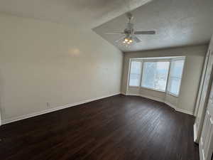 Empty room featuring a textured ceiling, lofted ceiling, dark wood-type flooring, and ceiling fan