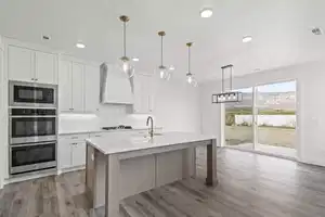 Kitchen with white cabinets, sink, an island with sink, custom range hood, and decorative light fixtures