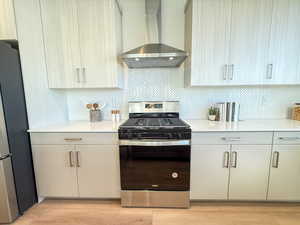 Kitchen with decorative backsplash, appliances with stainless steel finishes, light wood-type flooring, and wall chimney range hood