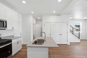 Kitchen featuring sink, white cabinetry, an island with sink, hardwood / wood-style flooring, and stainless steel appliances