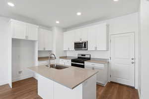 Kitchen with stainless steel appliances, an island with sink, sink, and white cabinetry